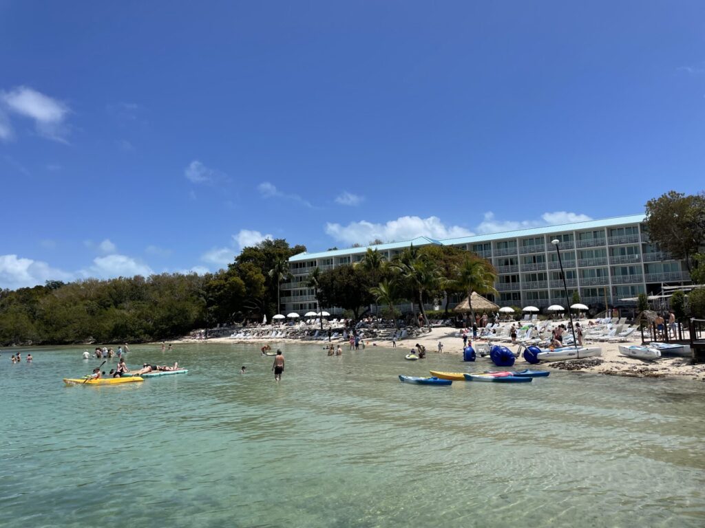 The beach at Baker's Cay Resort, some people lounging, others kayaking, with building in background, taken form he pier