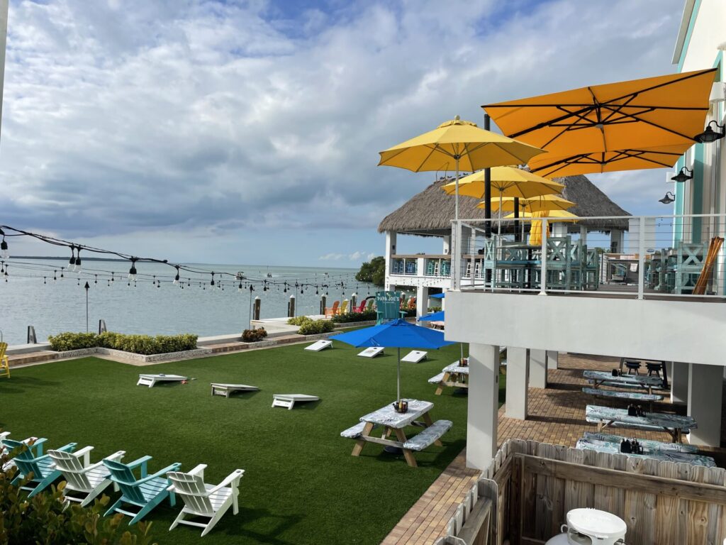 Outdoor seating at Papa Joe's Waterfront restaurant with astroturf grass, games, string lights, and balconies with umbrellas