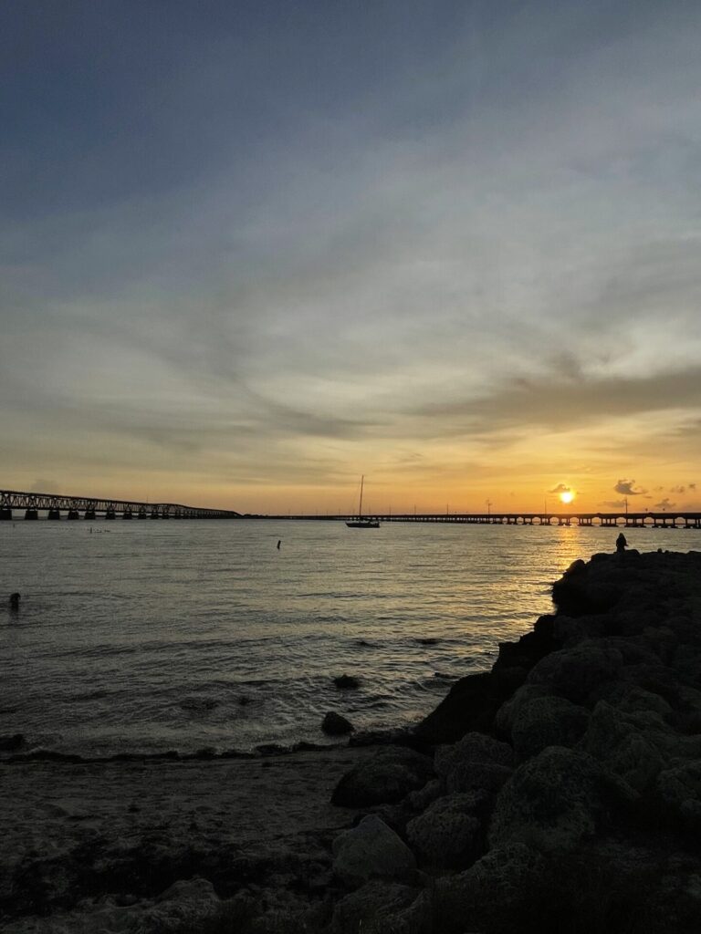 view of sunset, boat, beach, and bridge at Bahia Honda state park, a top attraction in the lower keys
