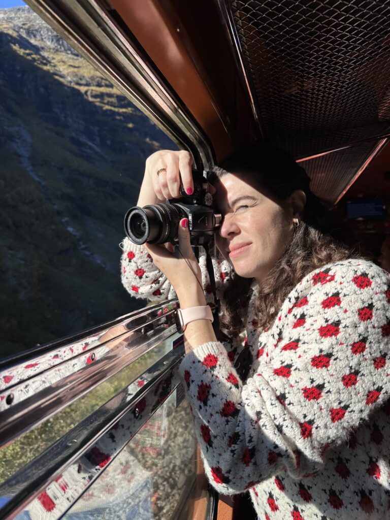 Natalie taking a photo with a camera out of a moving historic train with the window down in Norway
