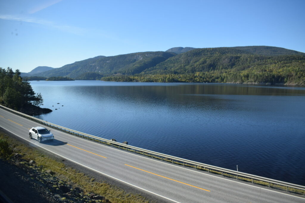view of a road, lake, and hill on a sunny day on the train from Oslo to Myrdal on Norway in a nutshell route